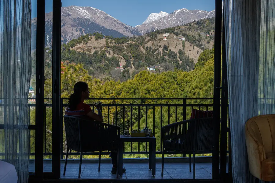A view of guest enjoying tea on a balcony overlooking the snow-capped Dhauladhar range at Rakkh Resort.