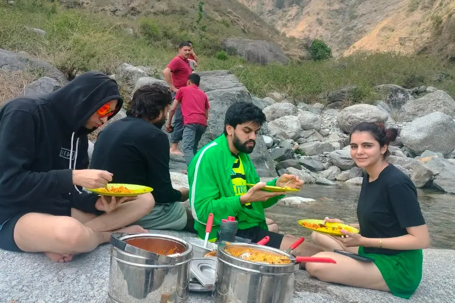 A view of guests enjoying an outdoor picnic meal by the riverside near Rakkh Resort.